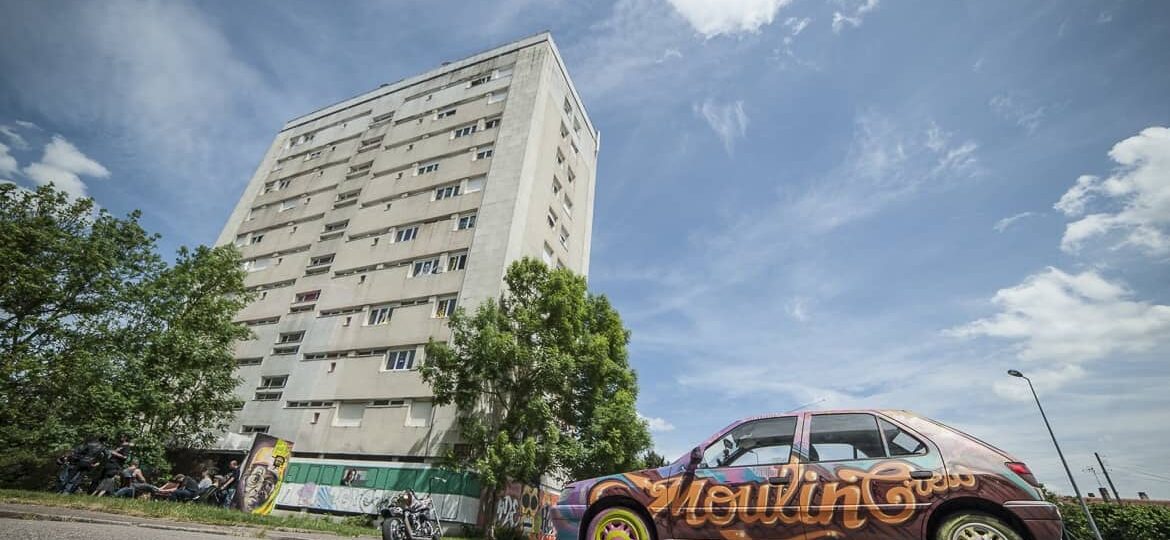 Immeuble et voiture graffée sous ciel bleu.