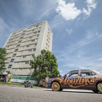 Immeuble et voiture graffée sous ciel bleu.