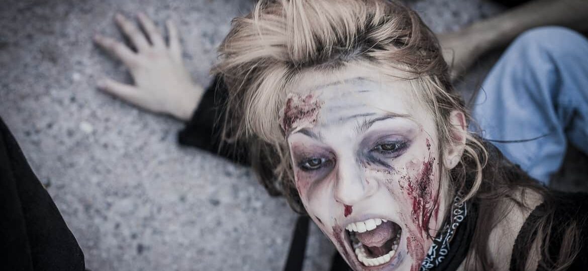 Personne maquillée en zombie effrayée au sol.