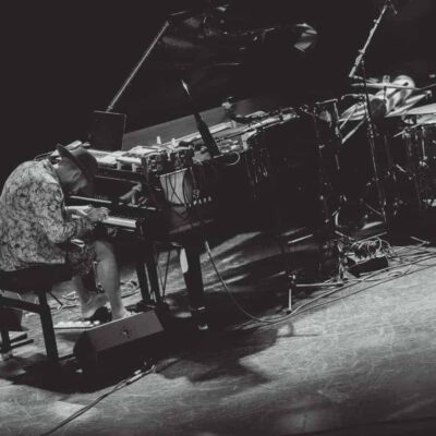 Musicien jouant du piano sur scène avec batterie.