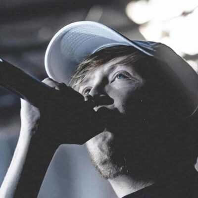 Chanteur avec microphone et casquette sur scène.