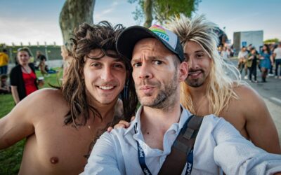 Trois hommes souriants prennent un selfie en extérieur.