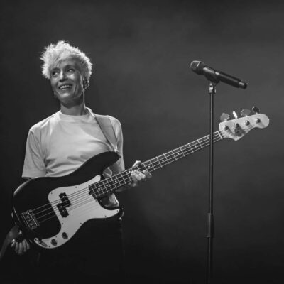 Musicienne souriante avec guitare basse sur scène.