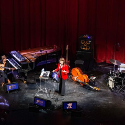Concert avec musiciens sur scène, instruments variés.