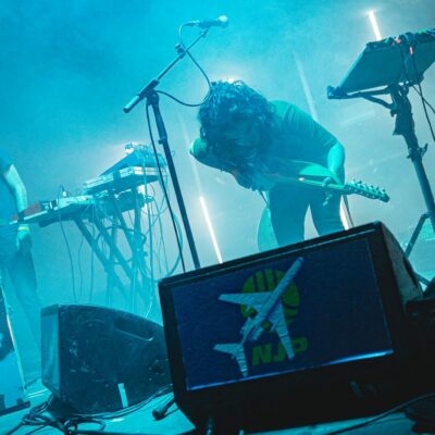 Concert avec synthétiseurs et guitare sur scène.
