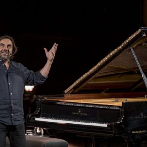 Homme souriant devant un piano à queue.