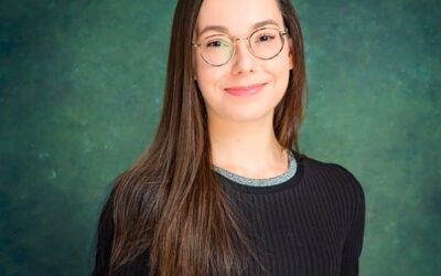 Femme souriante avec lunettes devant fond vert.