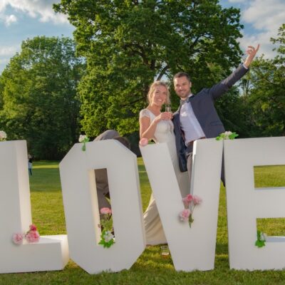 Couple joyeux devant lettres LOVE décorées de fleurs.