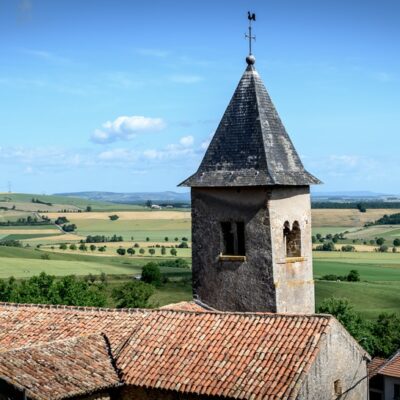 Église et campagne vallonnée sous ciel bleu.