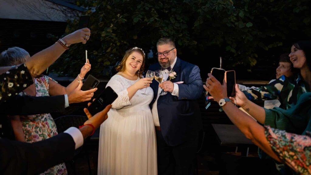 Mariage, couple trinque, invités prennent photos.