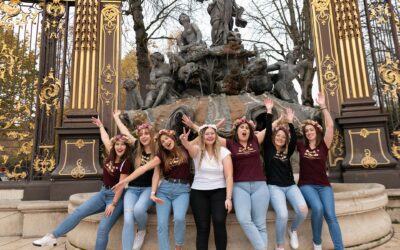 Groupe de femmes souriant devant une fontaine ornée.