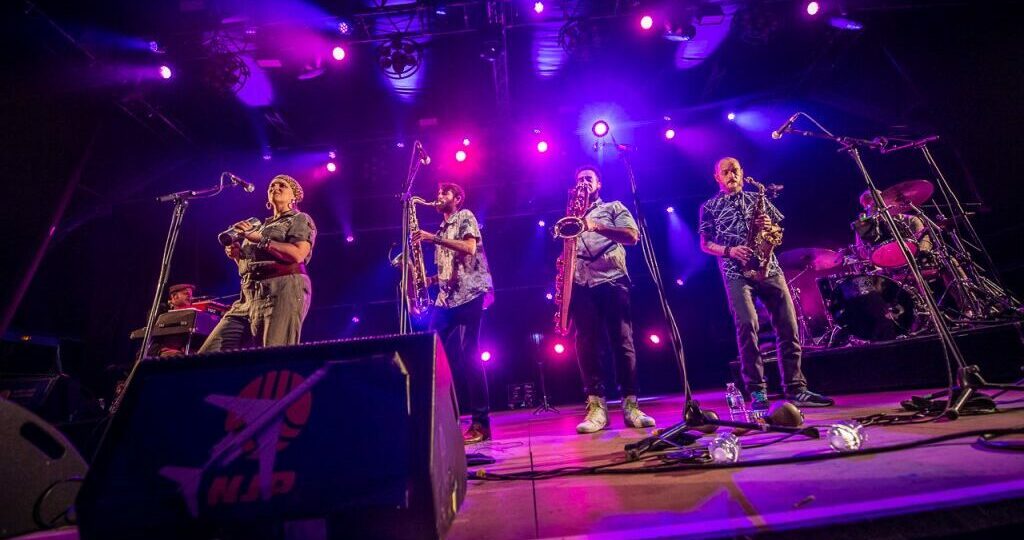 Groupe de musiciens en concert avec éclairage violet.