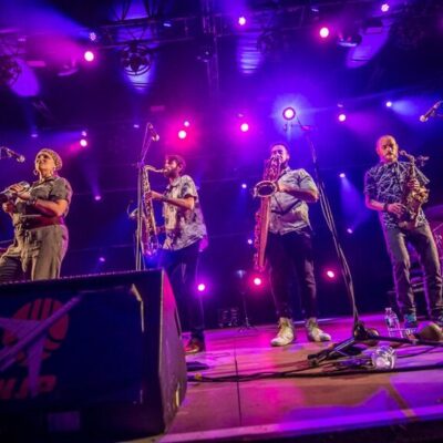 Groupe de musiciens en concert avec éclairage violet.
