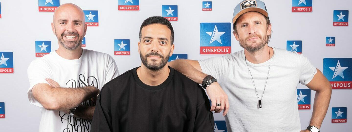 Trois hommes devant un fond Kinepolis.