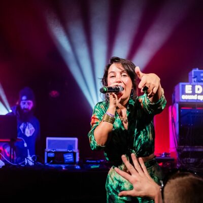 Chanteuse sur scène avec éclairage vibrant et DJ.