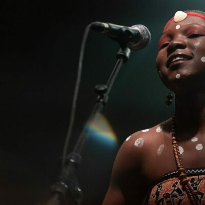 Chanteuse sur scène, micro et décorations corporelles.