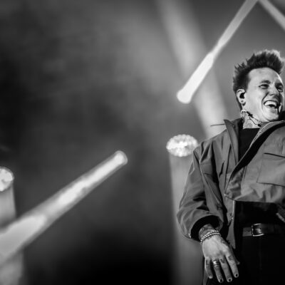 Chanteur souriant sur scène en concert noir et blanc.