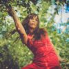 Femme en robe rouge dans un jardin ensoleillé.