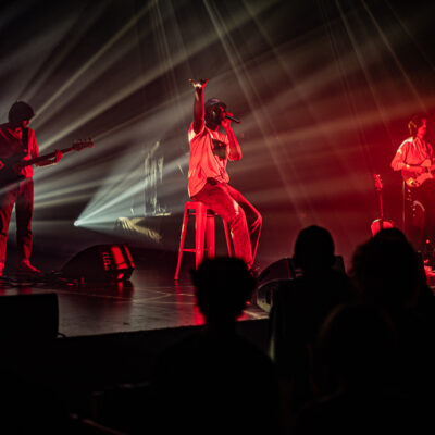 Groupe musical en concert, éclairages rouges et blancs.