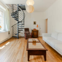 Salon avec escalier en colimaçon et canapé blanc.