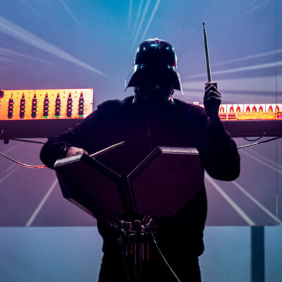 Musicien masqué jouant des percussions électroniques sur scène.
