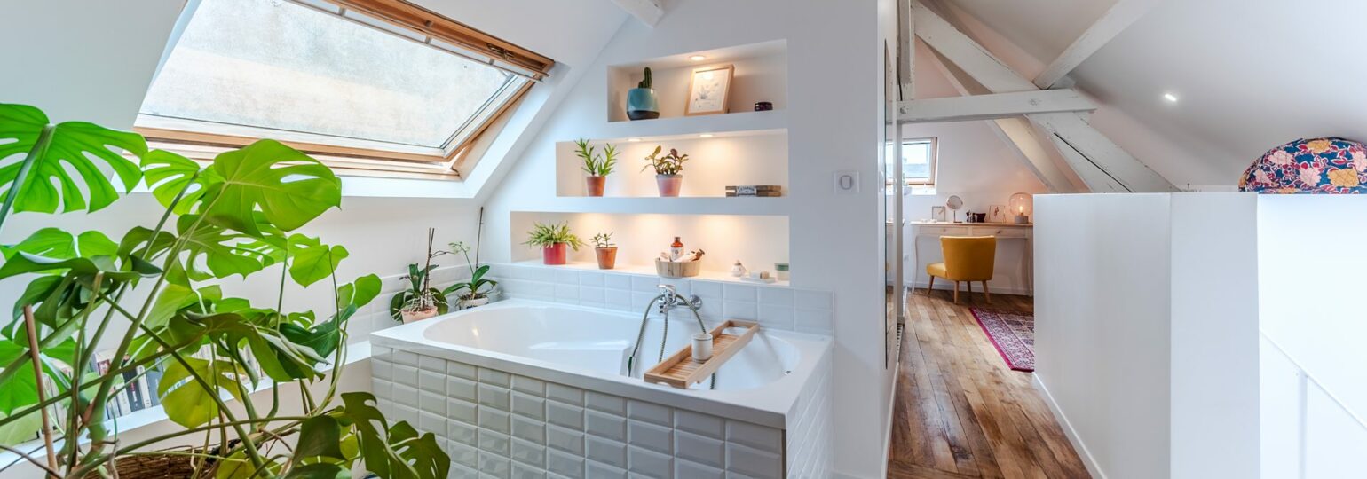Salle de bain lumineuse avec plantes et baignoire.