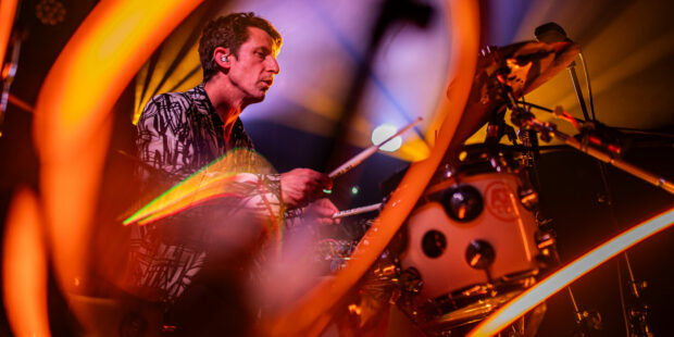 Batteur jouant sur scène sous éclairage coloré.