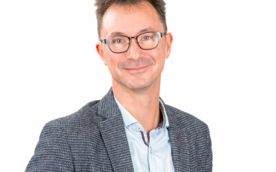 Personne souriante portant des lunettes et un blazer.