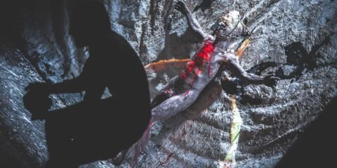 Silhouette devant sculpture ensanglantée sur fond sombre.