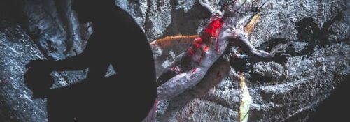 Silhouette devant sculpture ensanglantée sur fond sombre.