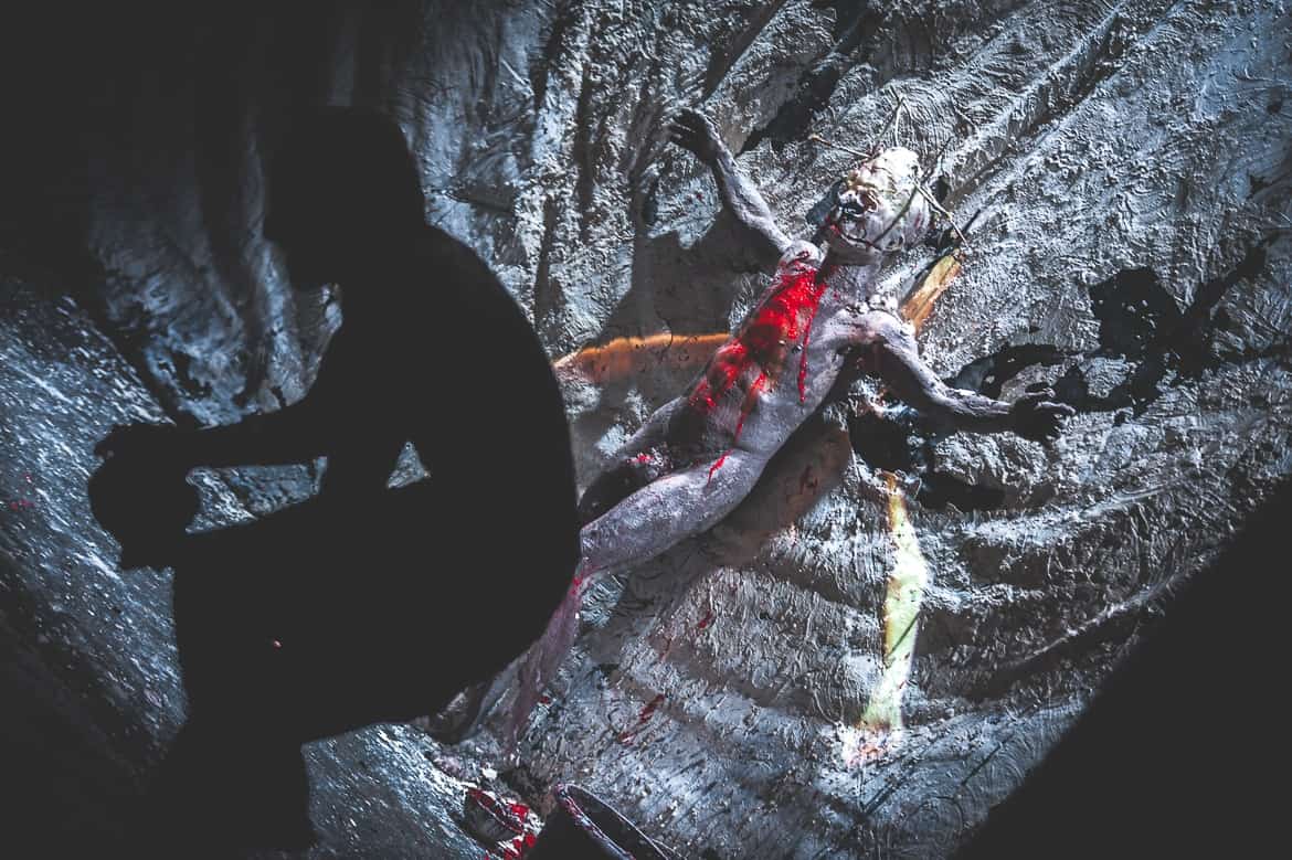 Silhouette devant sculpture ensanglantée sur fond sombre.