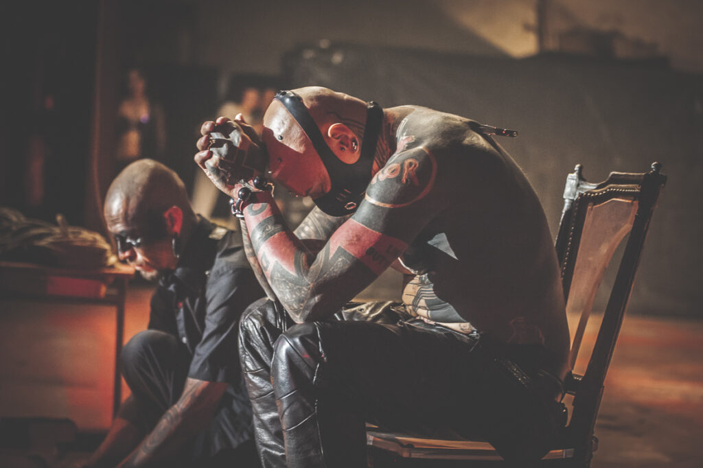 Deux hommes tatoués assis, ambiance mystérieuse.