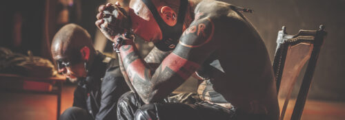 Deux hommes tatoués assis, ambiance mystérieuse.