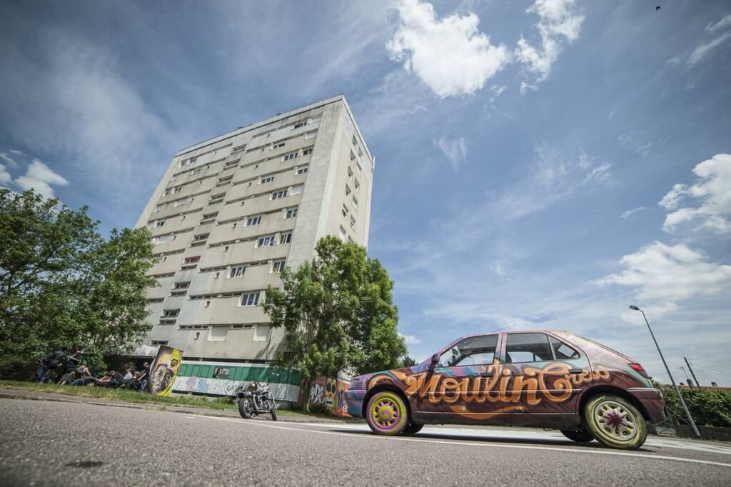 Immeuble et voiture graffée sous ciel bleu.