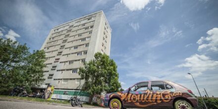 Immeuble et voiture graffée sous ciel bleu.