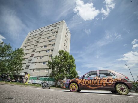 Immeuble et voiture graffée sous ciel bleu.