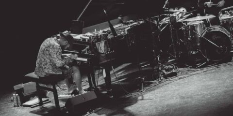 Musicien jouant du piano sur scène avec batterie.