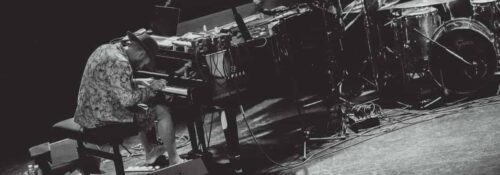 Musicien jouant du piano sur scène avec batterie.