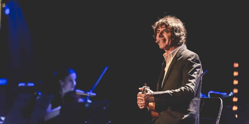 Homme souriant jouant de la guitare sur scène.