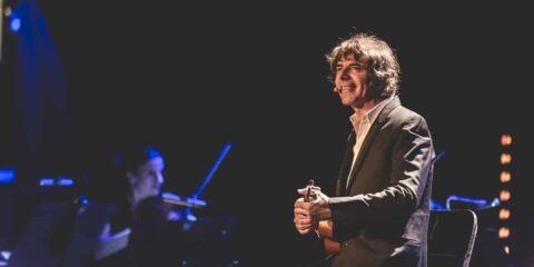 Homme souriant jouant de la guitare sur scène.