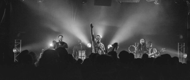 Groupe en concert sur scène avec éclairage lumineux.