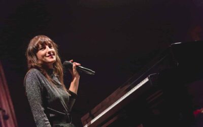 Femme souriant tenant un microphone, assise au piano.
