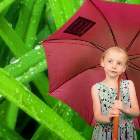 Fille avec parapluie rose, fond verdoyant.