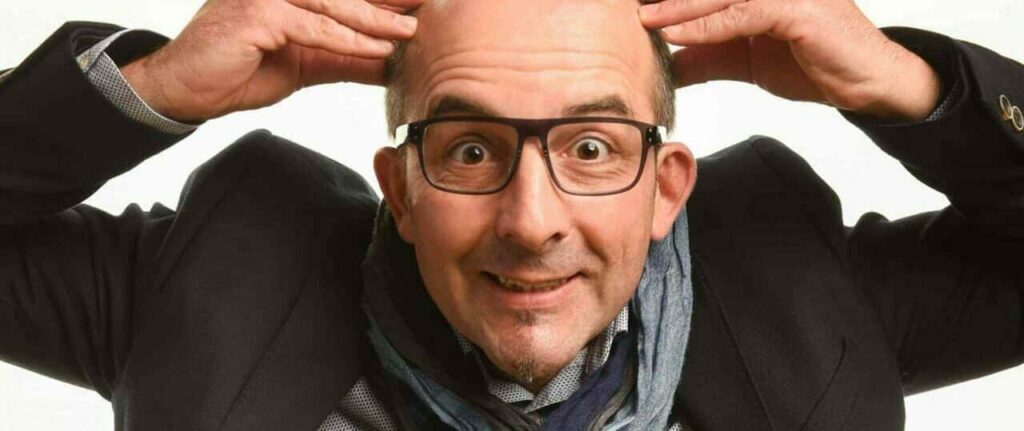 Homme chauve souriant touchant sa tête.