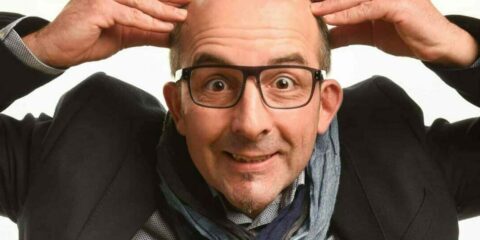 Homme chauve souriant touchant sa tête.