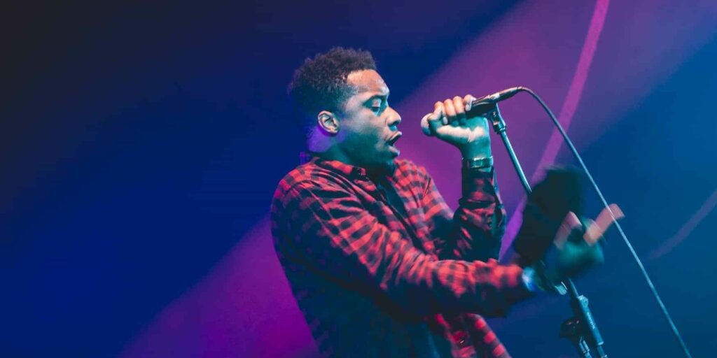 Musicien chante en concert, ambiance lumineuse.