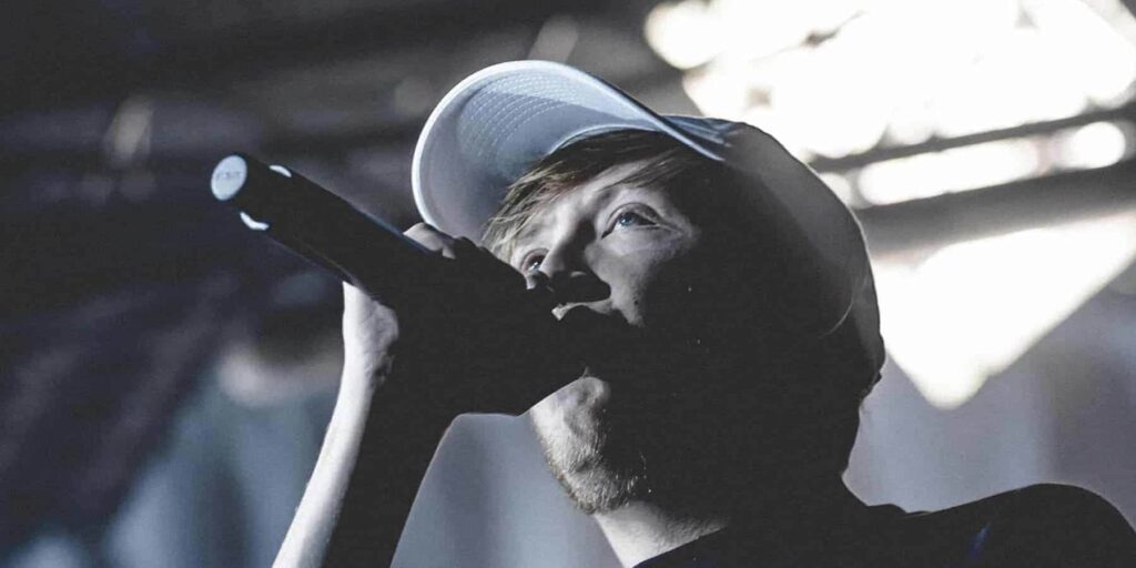 Chanteur avec microphone et casquette sur scène.