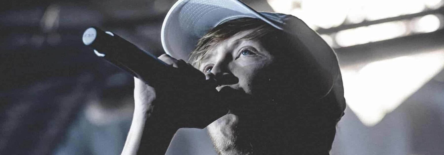 Chanteur avec microphone et casquette sur scène.