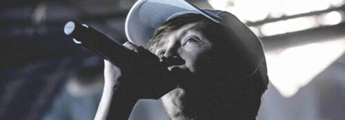 Chanteur avec microphone et casquette sur scène.