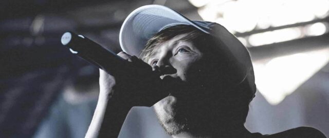 Chanteur avec microphone et casquette sur scène.